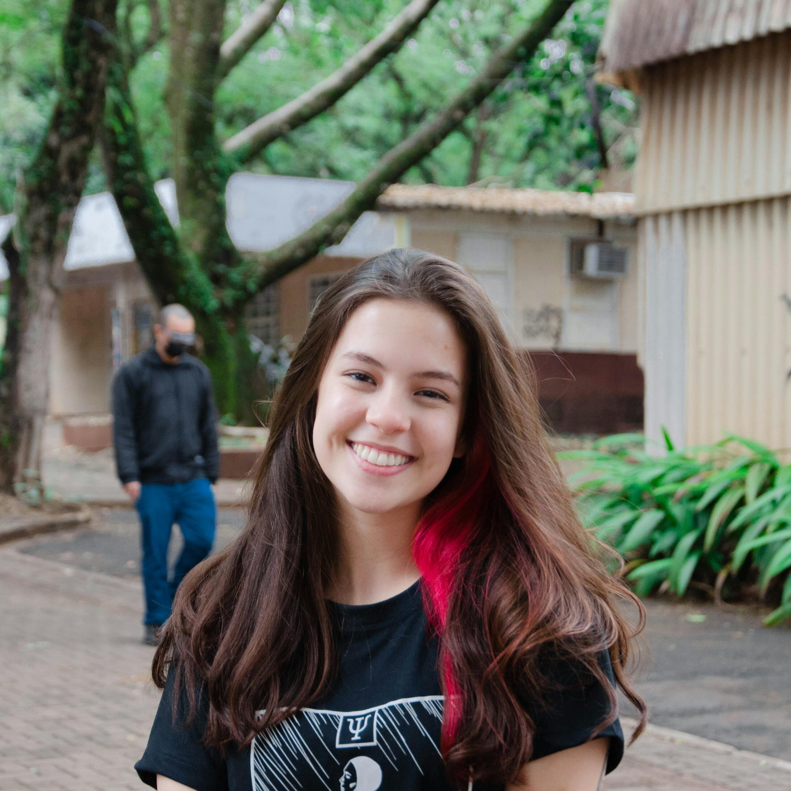 Home 11 Smiling teenager with long brown and pink hair in an outdoor setting, capturing youthful joy.