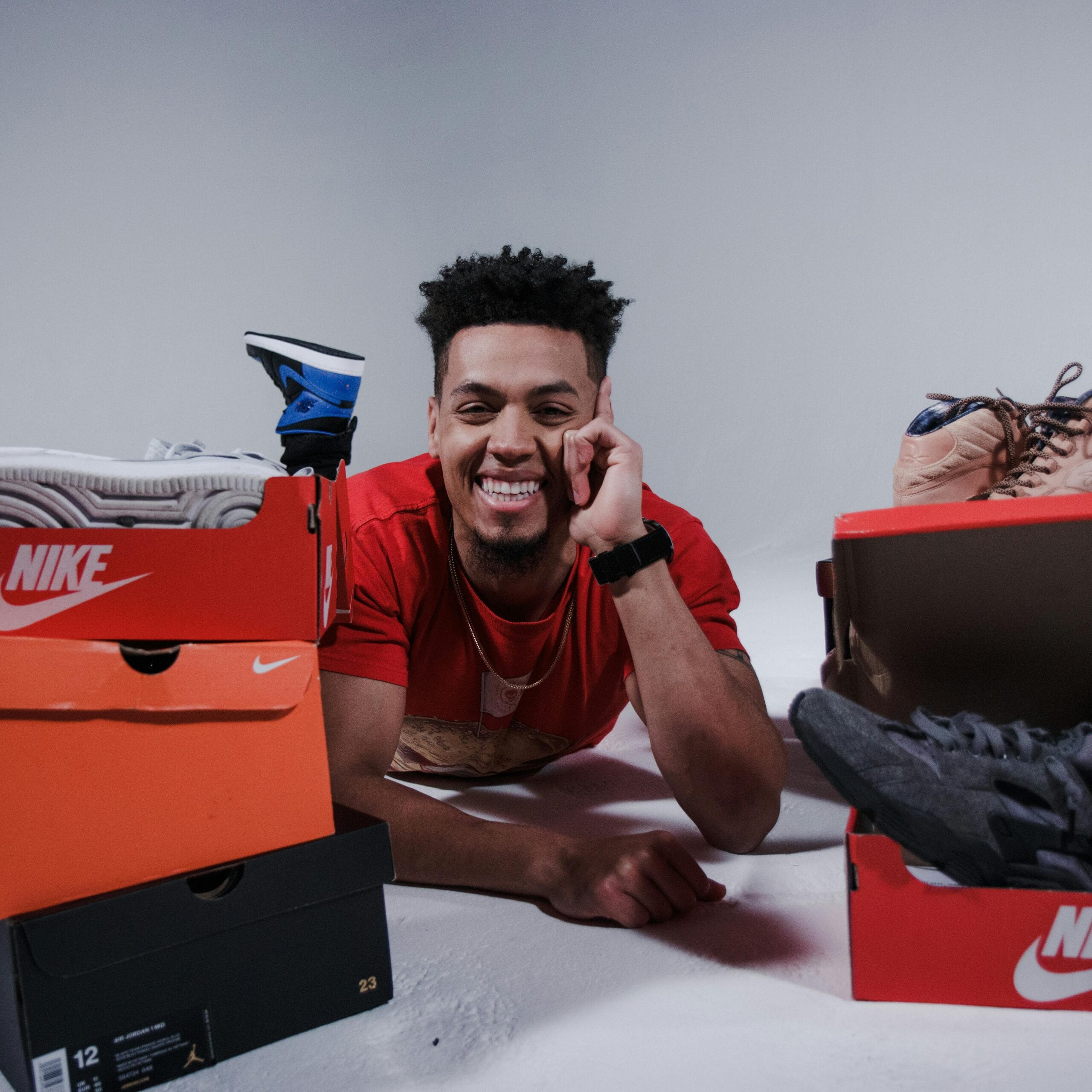 Home 15 Joyful man lying among various sneaker boxes, showcasing his collection.